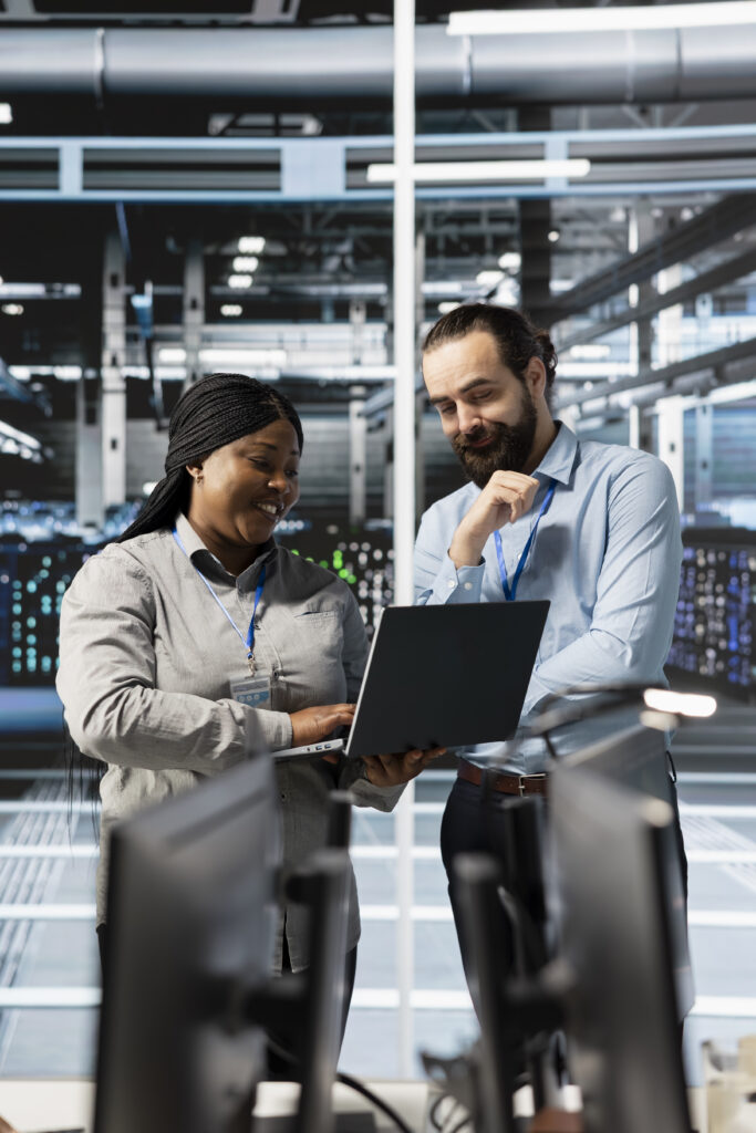 Cheerful team of engineers using laptop in server farm, analyzing data